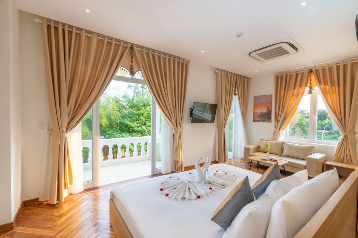 Ein Hotelzimmer mit einem großen Bett, einer Couch, einem Fernseher und einem Balkon mit Vorhängen.