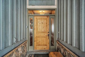 Eine hölzerne Haustür mit Glasschiebeelement, beides flankiert von Steinornamenten und einem Metallgeländer.