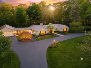 A modern house with a driveway, surrounded by lush greenery and trees.