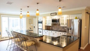 Een moderne keuken met een centraal eiland, roestvrijstalen apparatuur en hangende lampen.