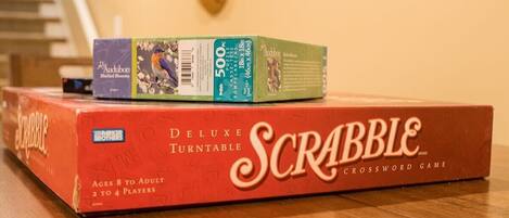 A Scrabble Deluxe Turntable game box on a wooden floor with a staircase and a small window in the background.