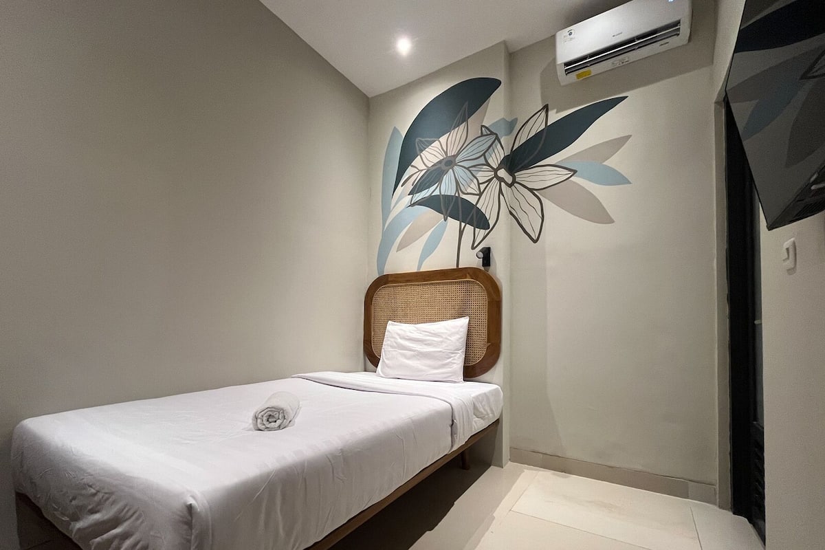 A single bed with a wooden headboard, a white pillow, and a wall-mounted air conditioner.