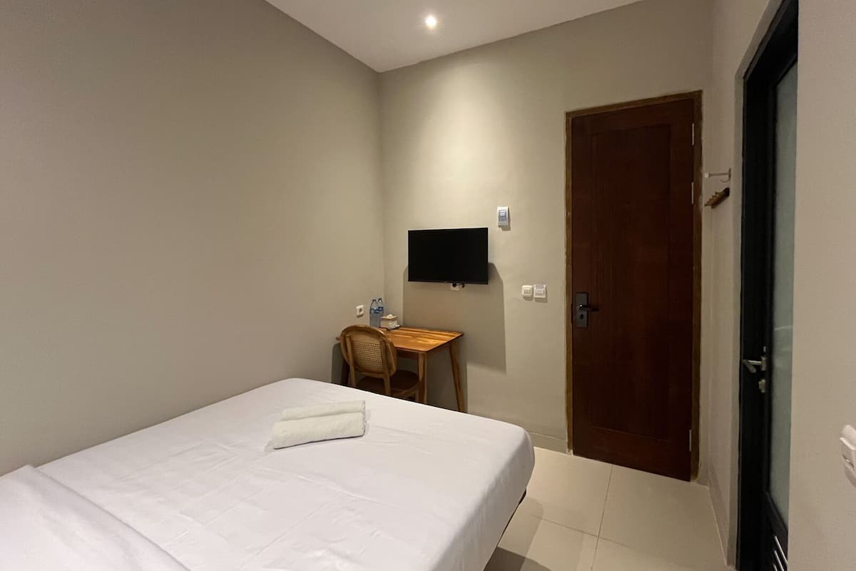 A hotel room with a single bed, a desk, a chair, a television, and a door.