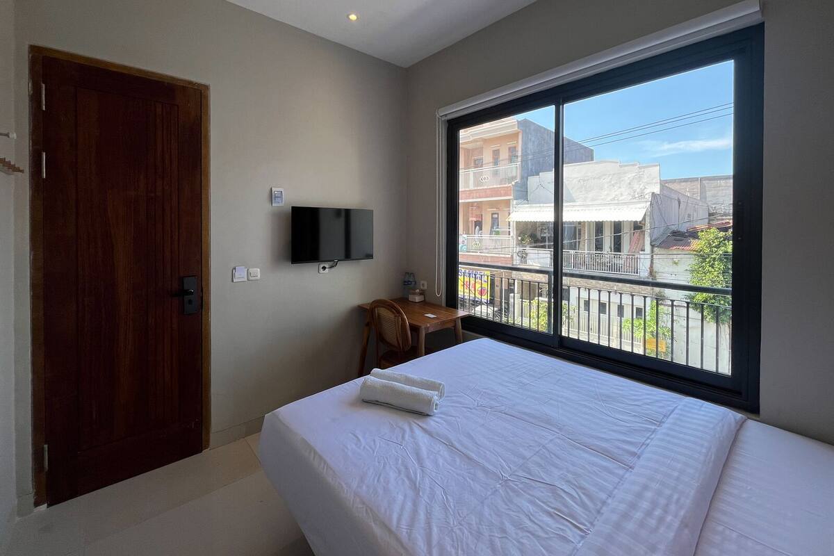 A hotel room with a large window, a bed, a desk, and a TV.