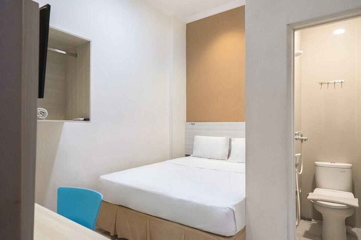 A small, single-bed room with a bed, a chair, a toilet, and a mirror.