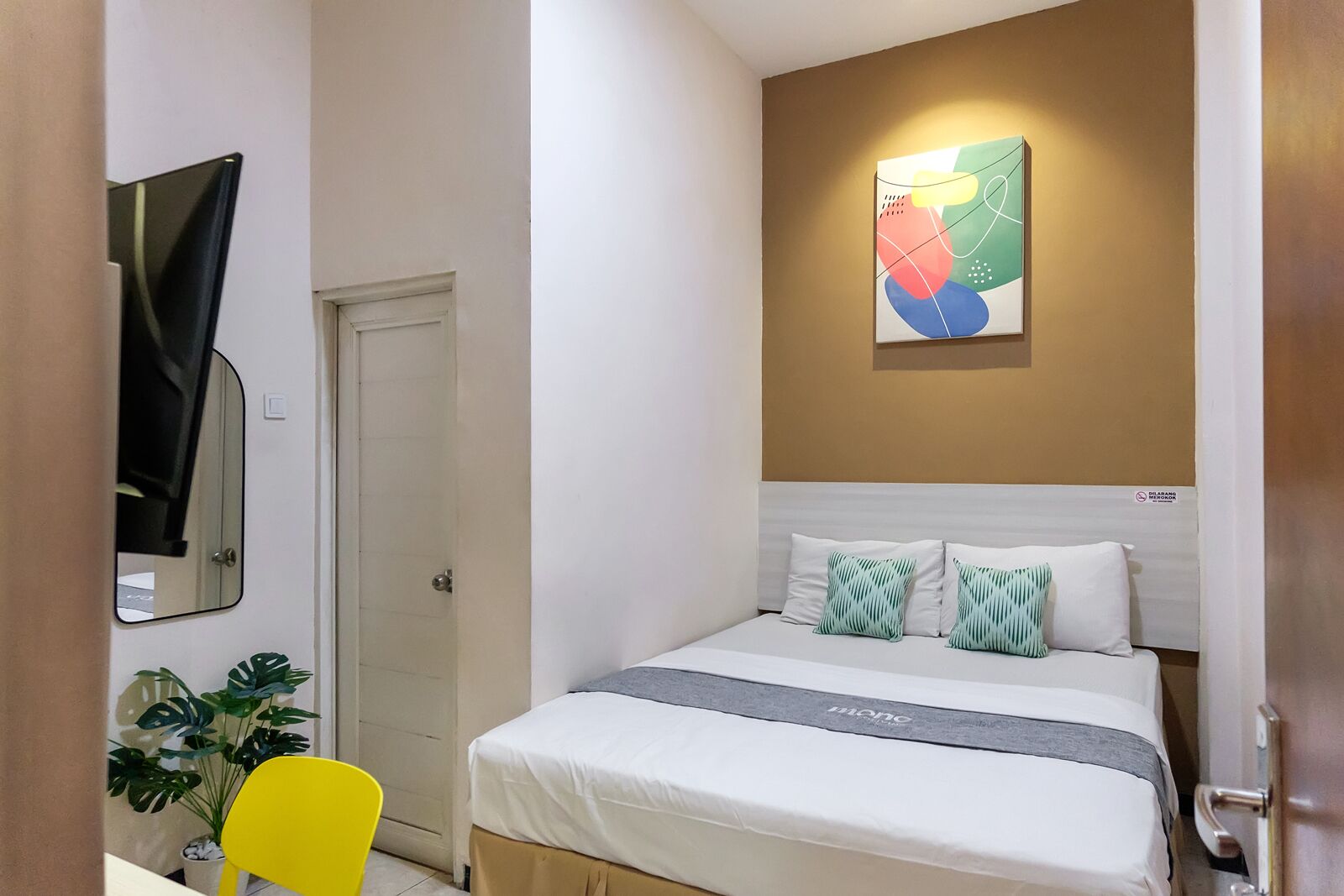 Une chambre d’hôtel avec un lit, un miroir, une plante et une œuvre d’art murale.
