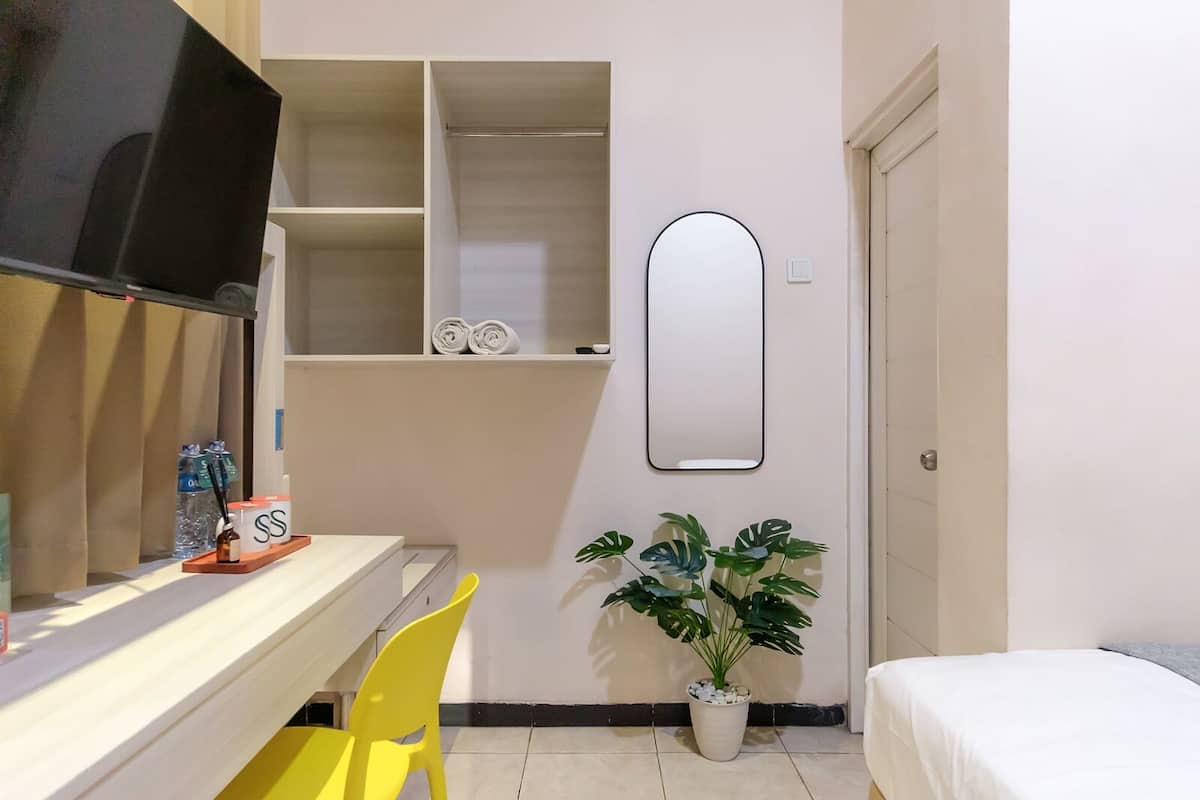 A hotel room with a bed, a desk with a chair, a TV, a mirror, and a potted plant.