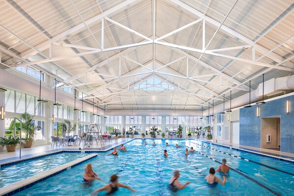 Swimmers enjoy the pool surrounded by multiple lanes and lush greenery.