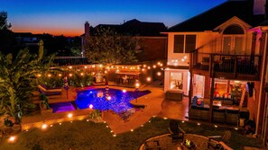 A backyard with a swimming pool, outdoor seating, and string lights.