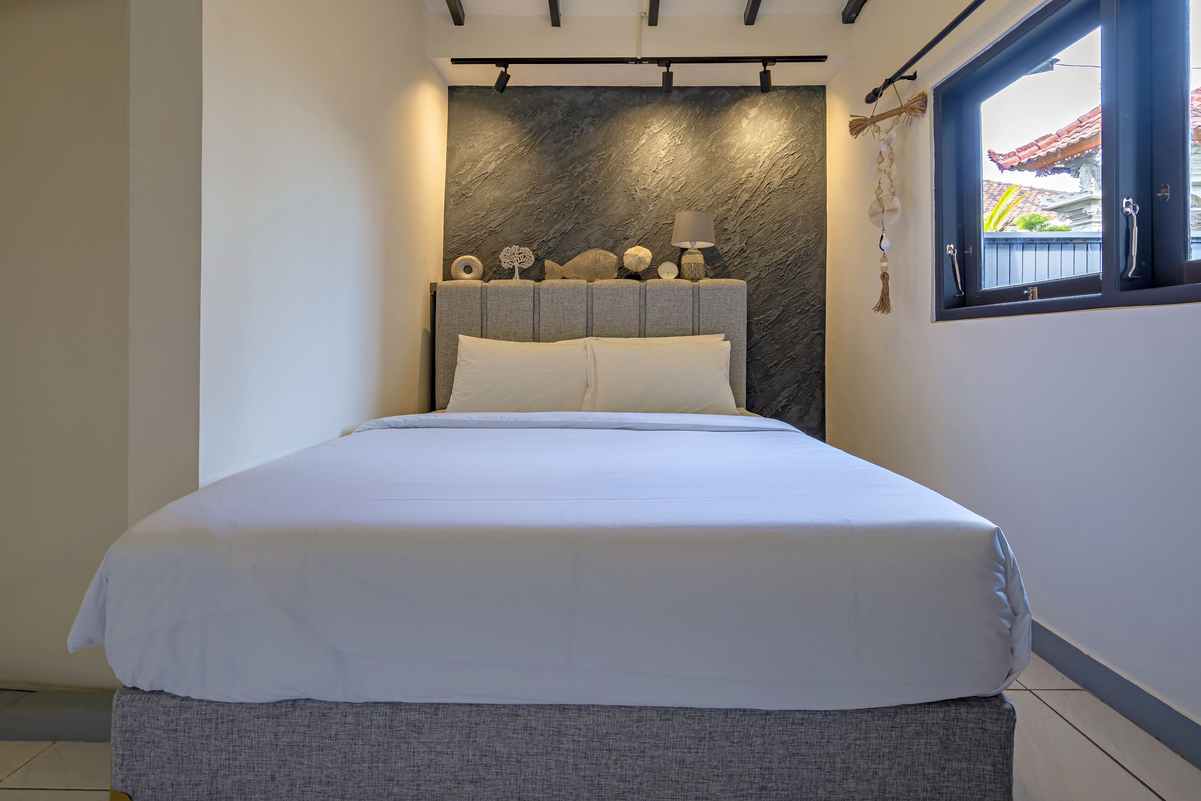 A neatly made bed with white linens, a grey headboard, and decorative items on top.