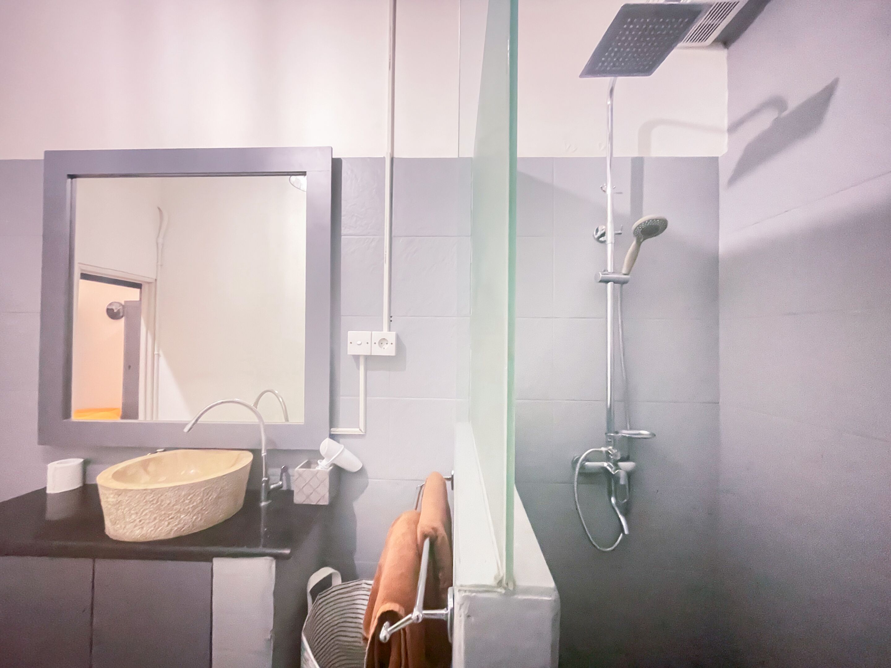 A modern bathroom with a large mirror, a round sink, a towel rack, and a shower with a handheld showerhead.