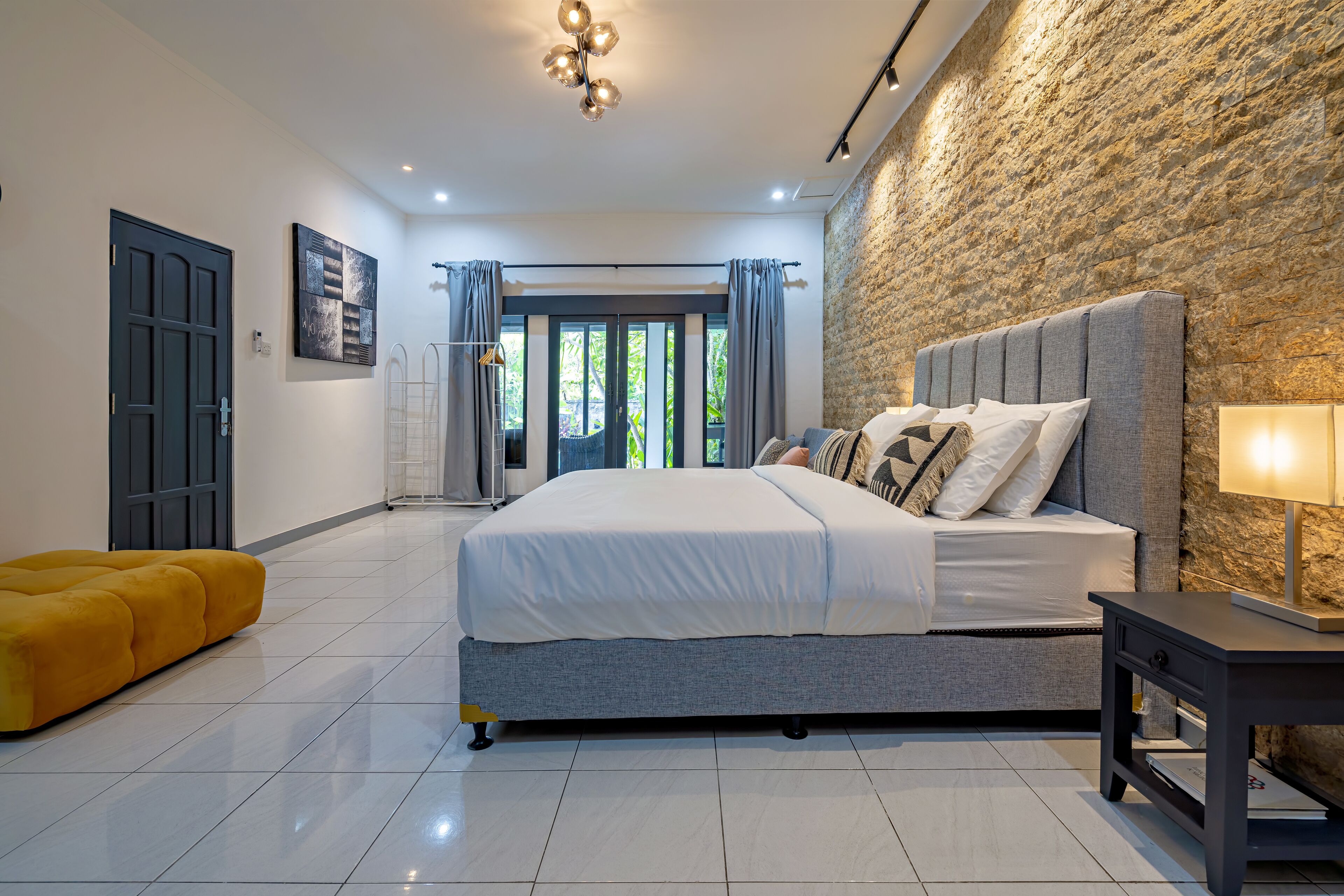 Un dormitorio moderno con una cama grande, un muro de piedra decorativo y una habitación luminosa y bien iluminada.