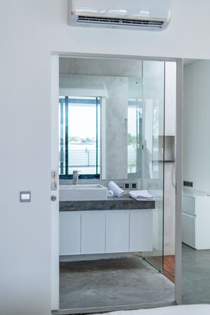 A modern bathroom with a glass shower enclosure, a large window, and a marble countertop. - Loft Carolyn (Canggu)