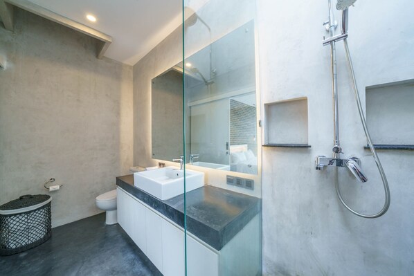 A modern bathroom with a glass shower enclosure, a white toilet, and a dual sink vanity. - Loft Carolyn (Canggu)
