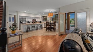 Una cocina moderna con una isla central, un comedor con sillas de madera y vistas a una piscina a través de puertas de cristal.