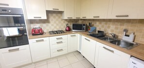 Fully equipped kitchen with microwave, toaster, gas stove, sink, and dish rack.