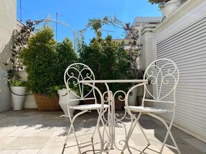A white metal table and chairs in an outdoor patio area with potted plants and a white building in the background. - Luxury (Monopoli)