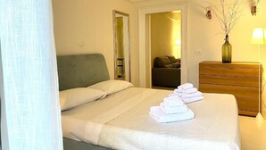 Hotellihuone, jossa on sänky, lipasto, peili ja maljakko, jossa on oksia.