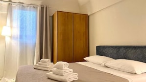 A hotel room with a bed, a wooden wardrobe, and a window with curtains.