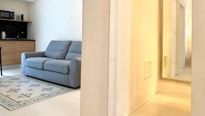 A modern living room with a grey sofa, a patterned rug, and a kitchen area with a microwave and kettle.