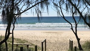 A sandy beach with a wooden bench and a path leading to the ocean. - The Pool Resort Kingscliff - One Bedroom Ocean and Pool View (4314) - Holiday Management Co. (Tweed)