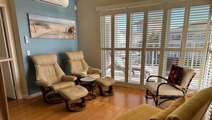 A room with a wooden floor, beige recliner chairs, a yellow sofa, and a window with blinds. - The Pool Resort Kingscliff - One Bedroom Ocean and Pool View (4314) - Holiday Management Co. (Tweed)