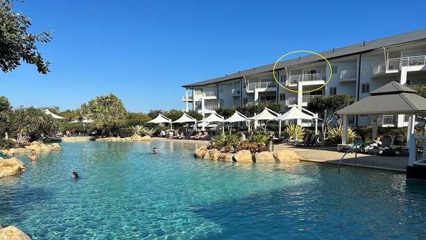 A swimming pool with clear water, surrounded by lounge chairs and umbrellas, and a building with balconies in the background. - The Pool Resort Kingscliff - One Bedroom Ocean and Pool View (4314) - Holiday Management Co. (Tweed)