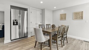 A modern kitchen with a stainless steel refrigerator, wooden dining table, and chairs.