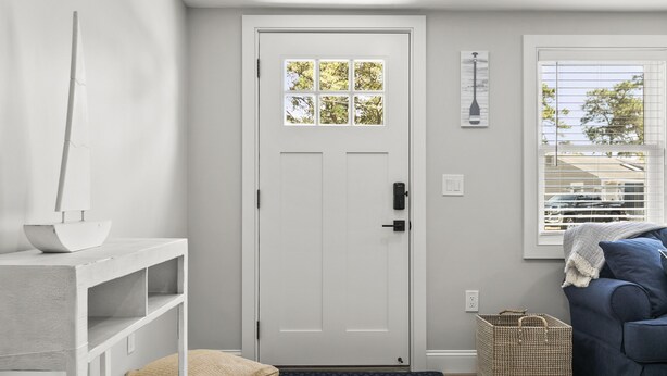 A modern entryway with a white door, a small bench, a blue sofa, and a wicker basket.