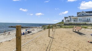 A beach with a volleyball net, a bench, and a house in the background.