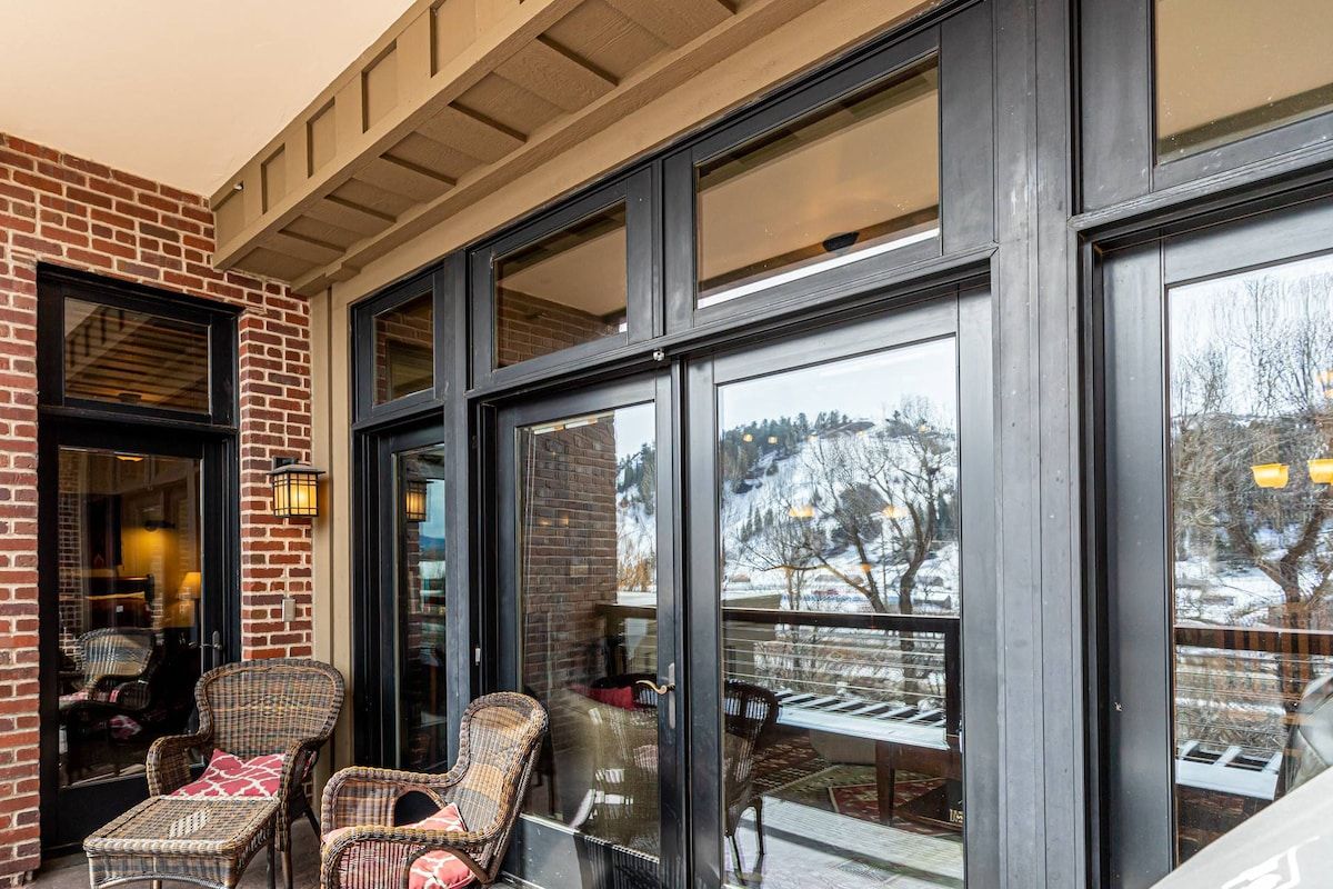 A brick building with large windows, wicker furniture, and a view of a snowy landscape.