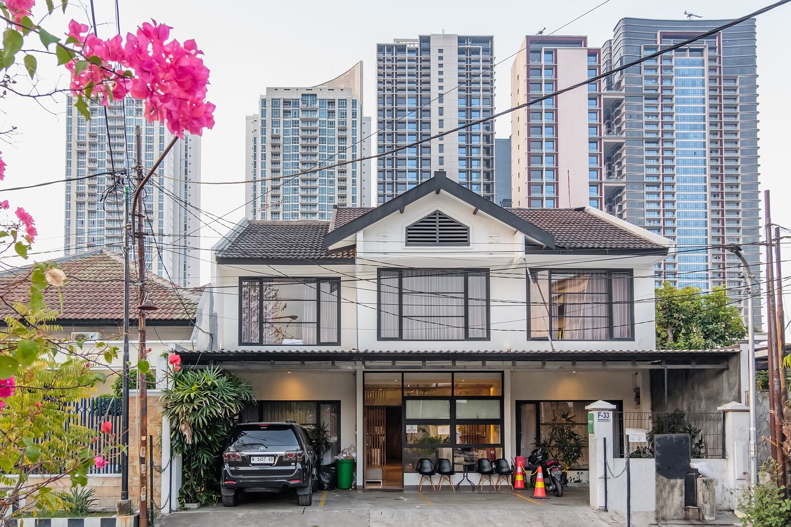 A two-story building with a garage, a car parked in front, and a row of chairs outside.