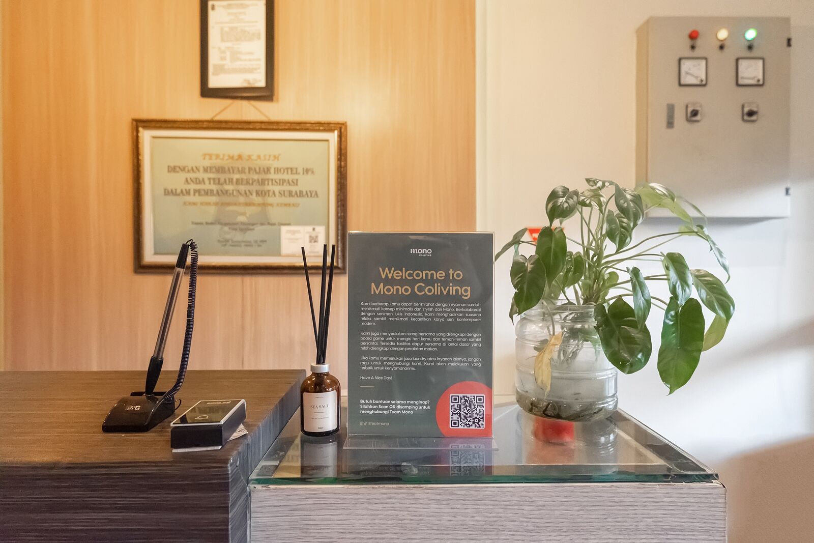 A reception desk with a framed certificate, a welcome sign, a plant, and a bottle of perfume.