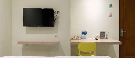 A hotel room with a bed, a desk with a chair, a television mounted on the wall, and a door.