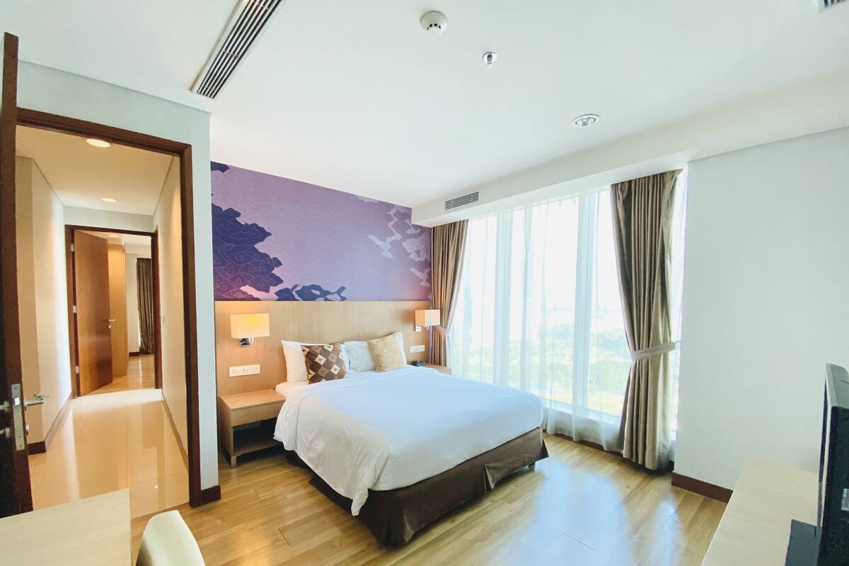 A hotel room with a large bed, a desk, a chair, a TV, and a view of the outdoors.