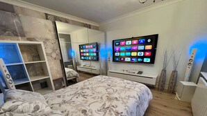 Ein modernes Schlafzimmer mit einem Bett, einem an der Wand montierten Fernseher, einem Kleiderschrank und einem Spiegel.