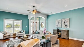 A living room with a teal wall, a ceiling fan, a large window, and a wooden floor. - Private Saltwater Heated Pool |8 Bikes |Walk to Johnson Beach |Single Level |Screened Lanai (Pensacola)