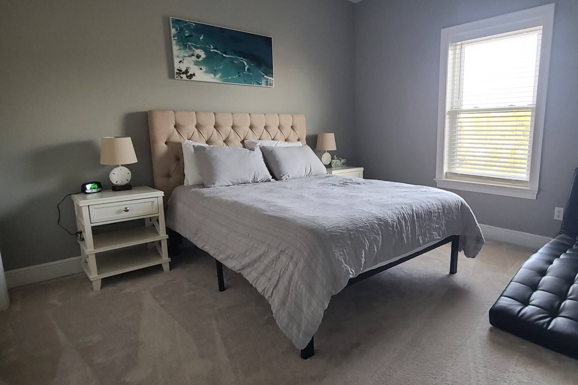 A bedroom with a large bed, two bedside tables, a nightstand, a window, and a black bench.