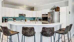 A modern kitchen with white cabinets, a large island with bar stools, stainless steel appliances, and teal backsplash. - Private Saltwater Heated Pool |8 Bikes |Walk to Johnson Beach |Single Level |Screened Lanai (Pensacola)