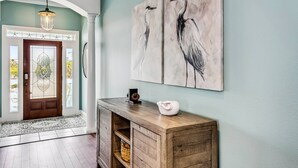 A hallway with a wooden console table, a door with a stained glass design, and two wall-mounted paintings of birds. - Private Saltwater Heated Pool |8 Bikes |Walk to Johnson Beach |Single Level |Screened Lanai (Pensacola)