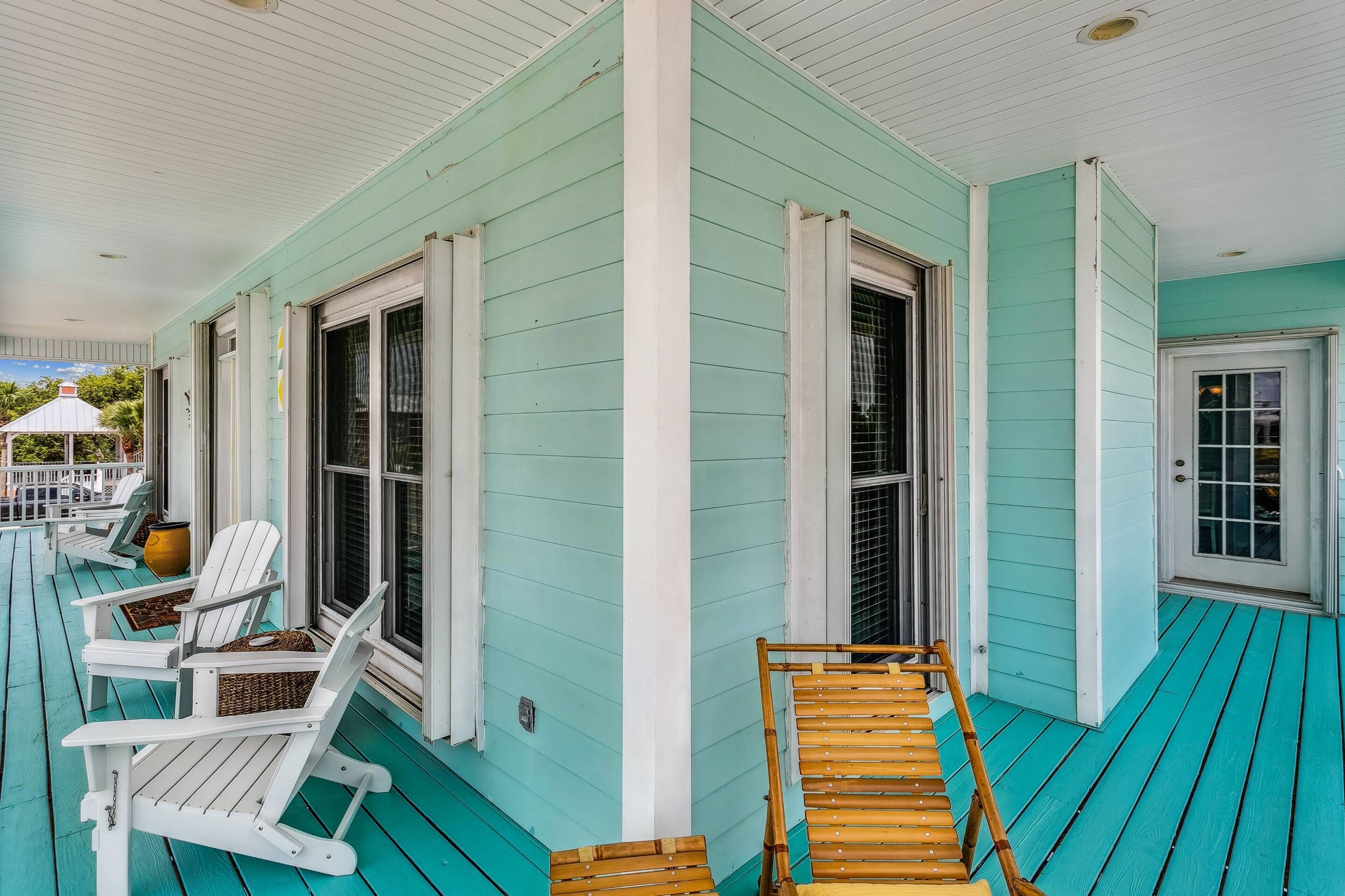 A turquoise wooden porch with white-framed windows and white railings.