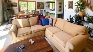 A spacious living room with a wooden ceiling, a large beige sectional sofa, a wooden coffee table, and a staircase with a wooden railing.
