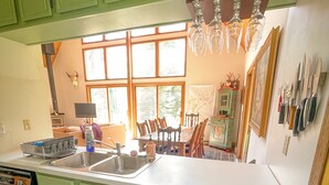 A kitchen with green cabinets, a large window, and a dining area with chairs.