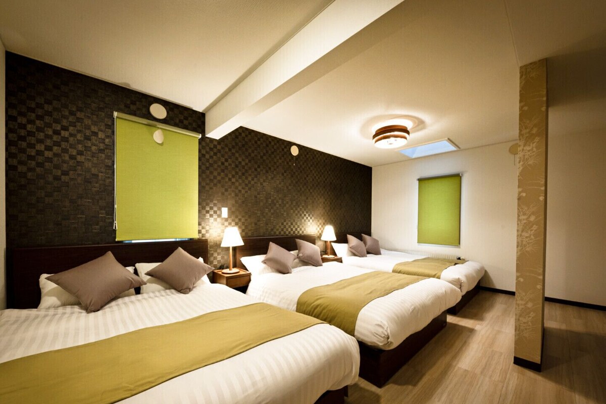 Habitación de hotel con tres camas, una pared a cuadros, un detalle en color verde y un tragaluz.
