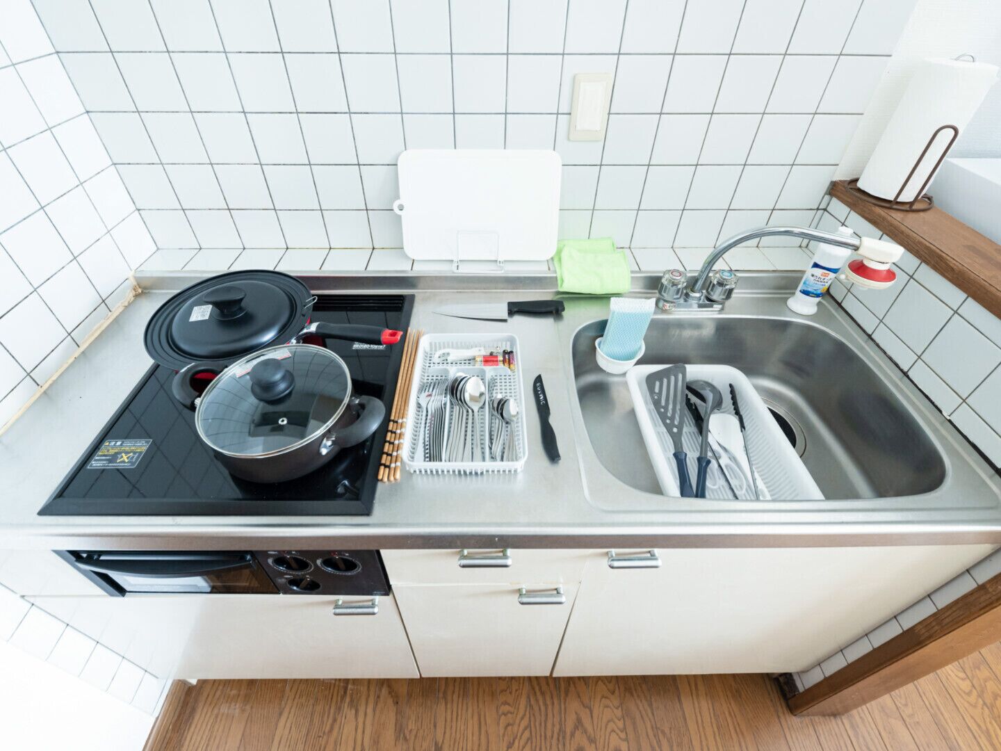 Eine kleine Küche mit Gaskochfeld, zwei Töpfen, Schneidebrett und Spüle mit Geschirrgestell.