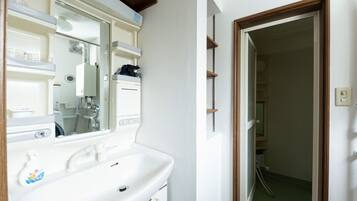 A bathroom with a white sink, mirror, and a shower visible through a door.
