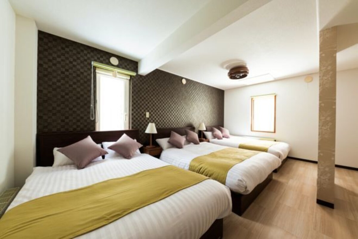 A hotel room with three beds, a large window, and a dark patterned wall.