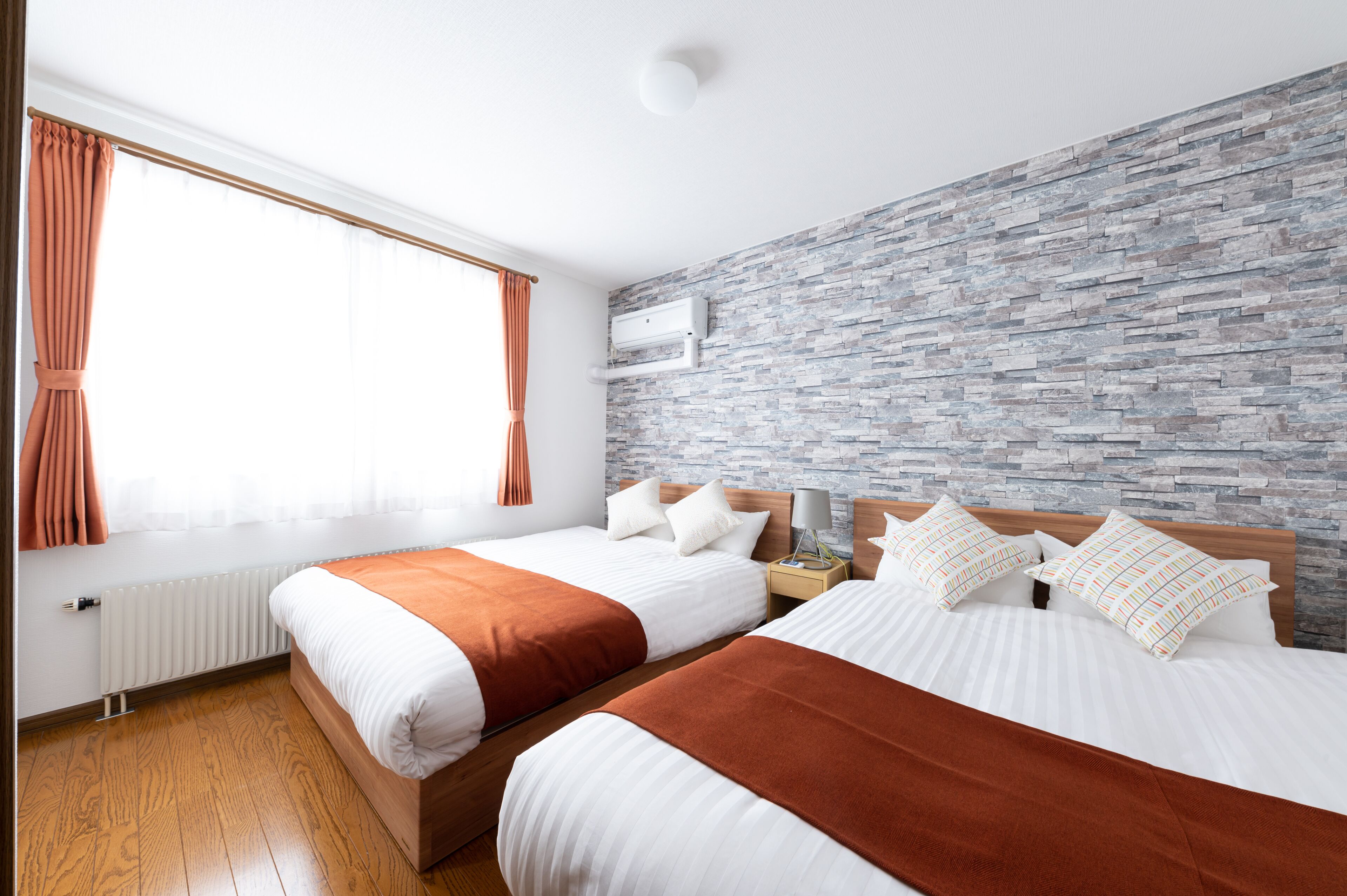 A hotel room with two beds, a stone-patterned wall, a window with curtains, and a radiator.