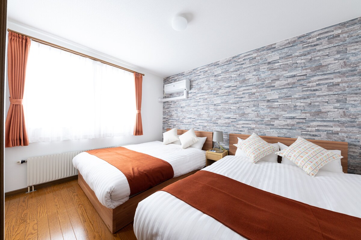 Habitación de hotel con dos camas, pared de piedra, ventana con cortinas y un radiador.