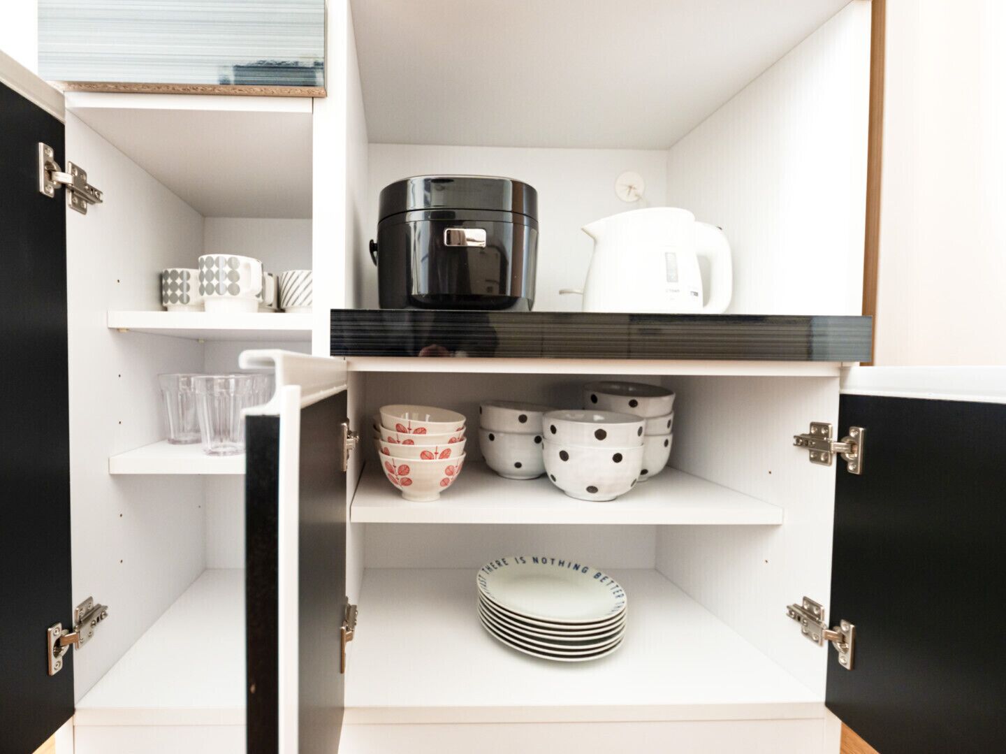 Een keuken met witte kastjes, een zwarte koffiezetapparaat, een witte waterkoker en verschillende kommen en borden.